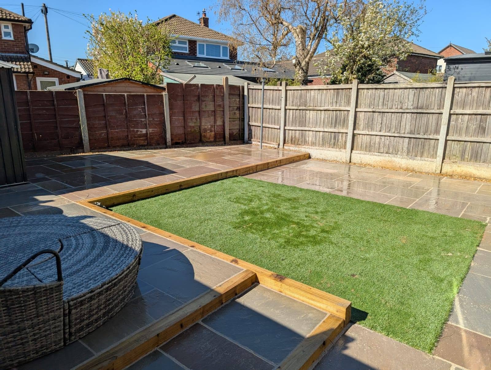 Natural sandstone patio with timber sleeper borders and a sunken artificial grass lawn