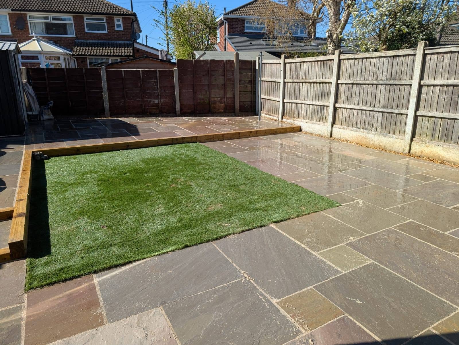 Wider view of a natural stone patio with a sleeper step and artificial grass
