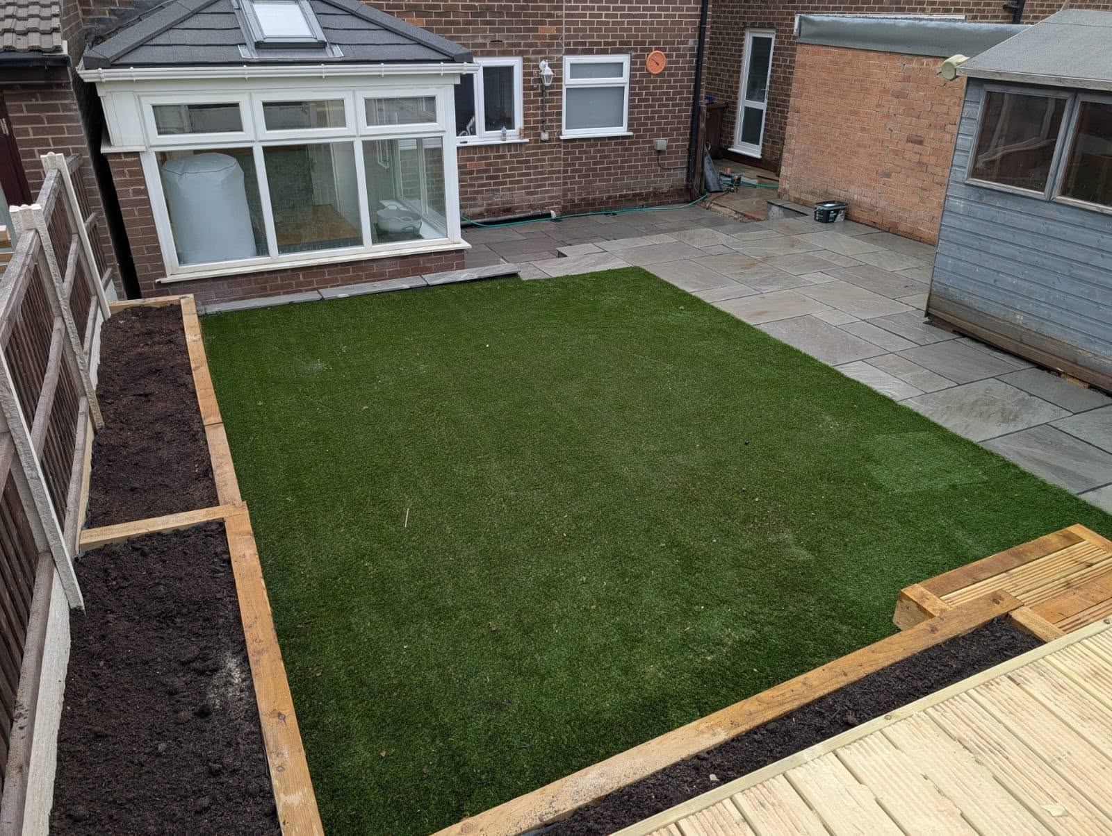 Tiered garden with artificial grass, timber sleeper planter beds and a paved patio